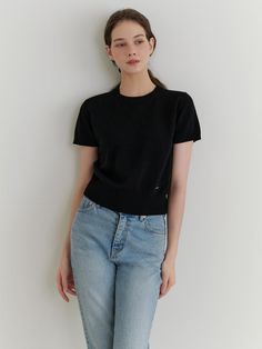 a woman standing in front of a white wall wearing jeans and a black t - shirt