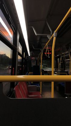 the interior of a bus with red seats and yellow railings at sunset or dawn