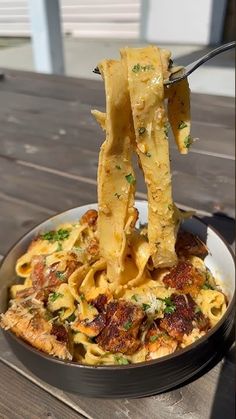 a bowl full of pasta being lifted with tongs from the top, on a wooden table