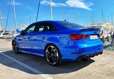 a blue car is parked in the parking lot next to some sailboats and boats