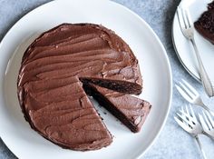 a chocolate cake on a white plate with one slice cut out and ready to be eaten