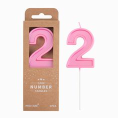 a pink candle with the number two on it in a cardboard box next to a white stick