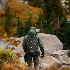 a man with a backpack is walking through the grass near some rocks and trees in the background