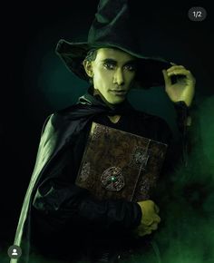 a woman dressed in green holding a book and wearing a witch's hat with her hands on her head