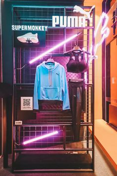 a display in a store with neon lights on the wall and clothes hanging from racks