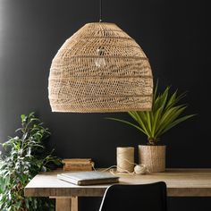 a wicker light hanging over a wooden table next to a potted green plant