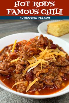 a white bowl filled with chili and cheese on top of a wooden table next to bread