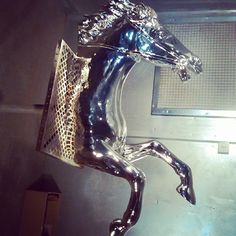 a shiny metal horse statue on display in a room with a light shining down the wall