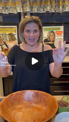 a woman standing in front of a wooden bowl holding her hands up to the camera