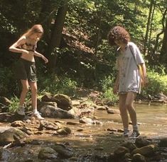 two people are standing in the water near some rocks and trees, one is holding a frisbee