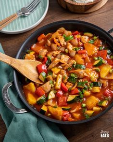 a skillet filled with vegetables and rice on top of a wooden table next to a bowl