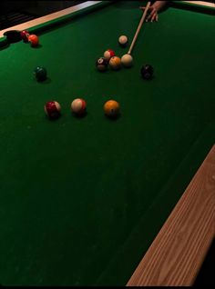 a pool table with several balls on it and a person holding a cue in their hand