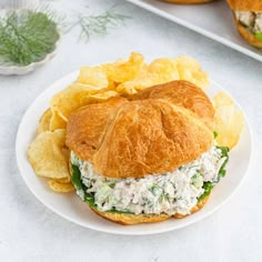 a chicken salad sandwich on a croissant bun with potato chips next to it