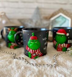 three christmas themed coffee mugs sitting next to a silver ball chain on a white blanket