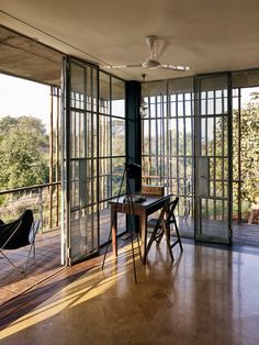 an empty room with glass walls and wooden flooring, overlooking the trees outside on a sunny day