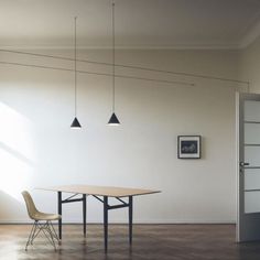 an empty room with a table and two chairs in front of the wall that has three hanging lights above it