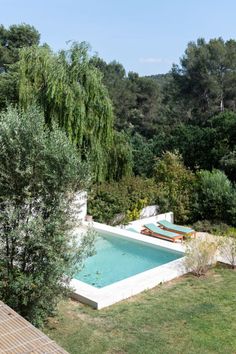 an outdoor swimming pool surrounded by trees and grass with lounge chairs on the lawn area