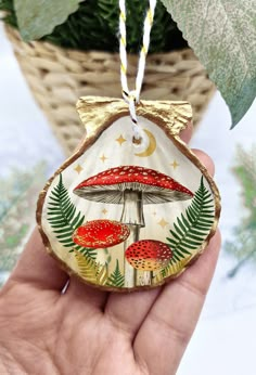 a hand holding a ceramic ornament with red mushrooms and green leaves on it