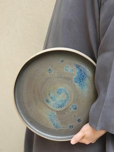 a person holding a gray plate with blue designs on the bottom and inside, in front of a beige wall