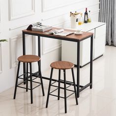 two stools and a table with drinks on it in front of a white wall