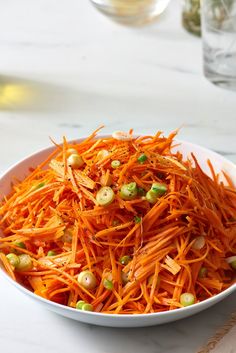 a white bowl filled with carrots and pistachio on top of a table