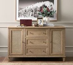 a wooden cabinet with drawers in front of a painting and pictures on the wall behind it