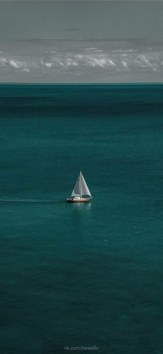 a lone sailboat in the middle of an ocean with dark blue water and white clouds