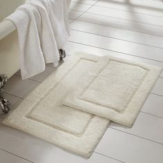 two bath mats sitting on the floor in front of a bath tub and towel rack