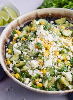 a bowl filled with vegetables and cheese on top of a table next to limes