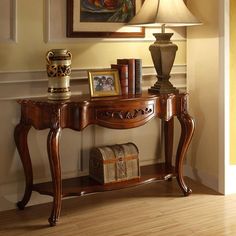 a wooden table with books on it next to a lamp and pictures hanging on the wall