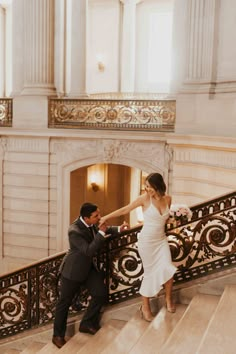 a bride and groom walking down the stairs at their wedding reception in an ornate building