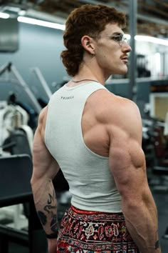 a man with glasses and no shirt on in a gym looking off to the side