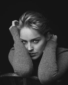 a black and white photo of a woman with her hands on her head, leaning against a chair