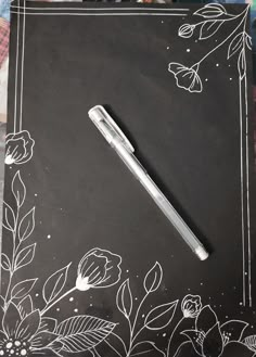 a pen sitting on top of a black paper with white flowers and leaves around it