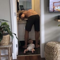 a man standing over a baby who is laying on the floor in front of a mirror