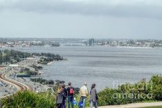 three people are standing on the edge of a hill looking out at the ocean and highway