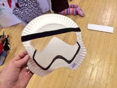 a person holding a paper plate with a mask on it's face in the middle of a wooden floor