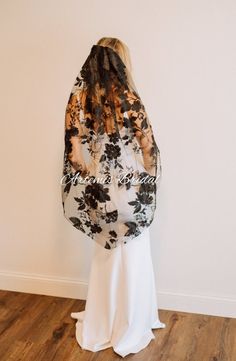 a woman standing in front of a wall wearing a black and white dress with flowers on it