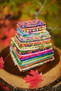 a stack of multicolored fabric sitting on top of a tree stump next to leaves