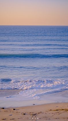 a person walking on the beach with a surfboard in hand and an ocean in the background