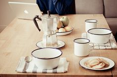 a wooden table topped with plates and cups filled with food next to a laptop computer