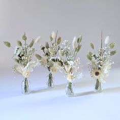 three vases filled with white flowers and greenery