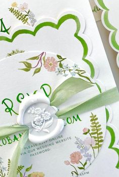 the wedding stationery is decorated with green and white flowers, ribbons, and monogrammings