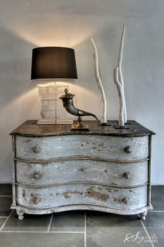 an old dresser with some branches on top and a lamp next to it in the corner