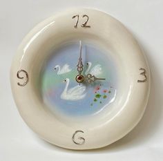 a white clock with two swans on it's face and numbers in the middle