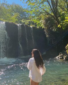 a woman standing in front of a waterfall with her back to the camera and looking at it