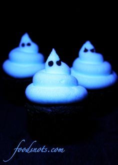 three cupcakes with white frosting and black eyes on them in the dark