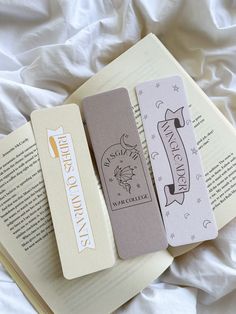 three bookmarks sitting on top of an open book next to a white bed sheet