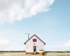 a small white house sitting on top of a sandy beach under a blue cloudy sky