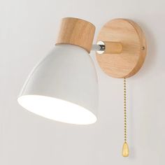 a wooden wall light with a white shade on it's face and chain hanging from the side